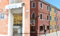 A split screen image of a pink walled shop in Murano on the left and colourful buildings in Burano on the right in Venice, Italy. Photo copyright and credit: Author