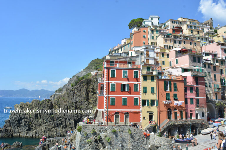 A medium shot of the red building in Riomaggiore in Cinque Terre in Italy showing the buildings on the cliffs. In the background is a cloudless blue summer sky.