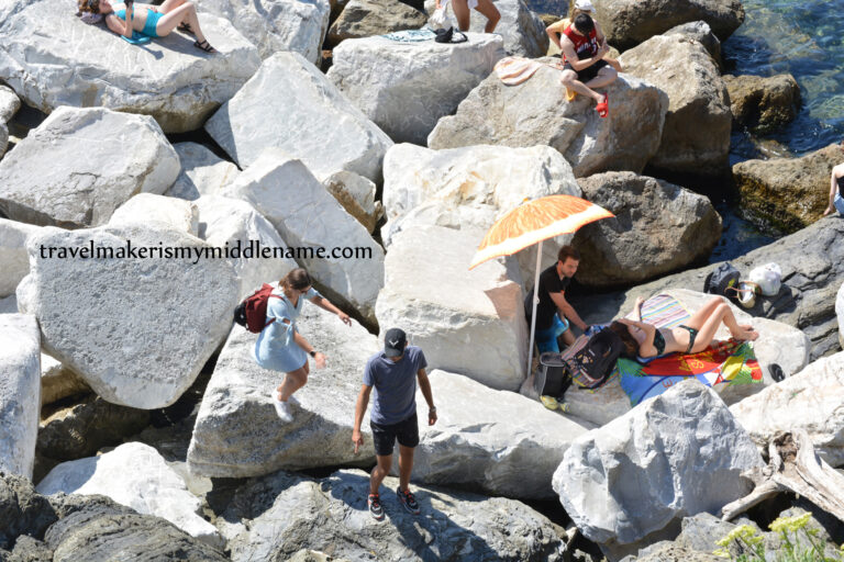 People sunbaking on large white rocks in Riomaggiore, Italy.