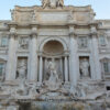 A front view of the Trevi Fountain during the day time with a blue cloudless sky in the top.