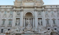 A front view of the Trevi Fountain during the day time with a blue cloudless sky in the top.