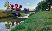 A small farm tractor crossing a small bridge tows a large parade float behind it.