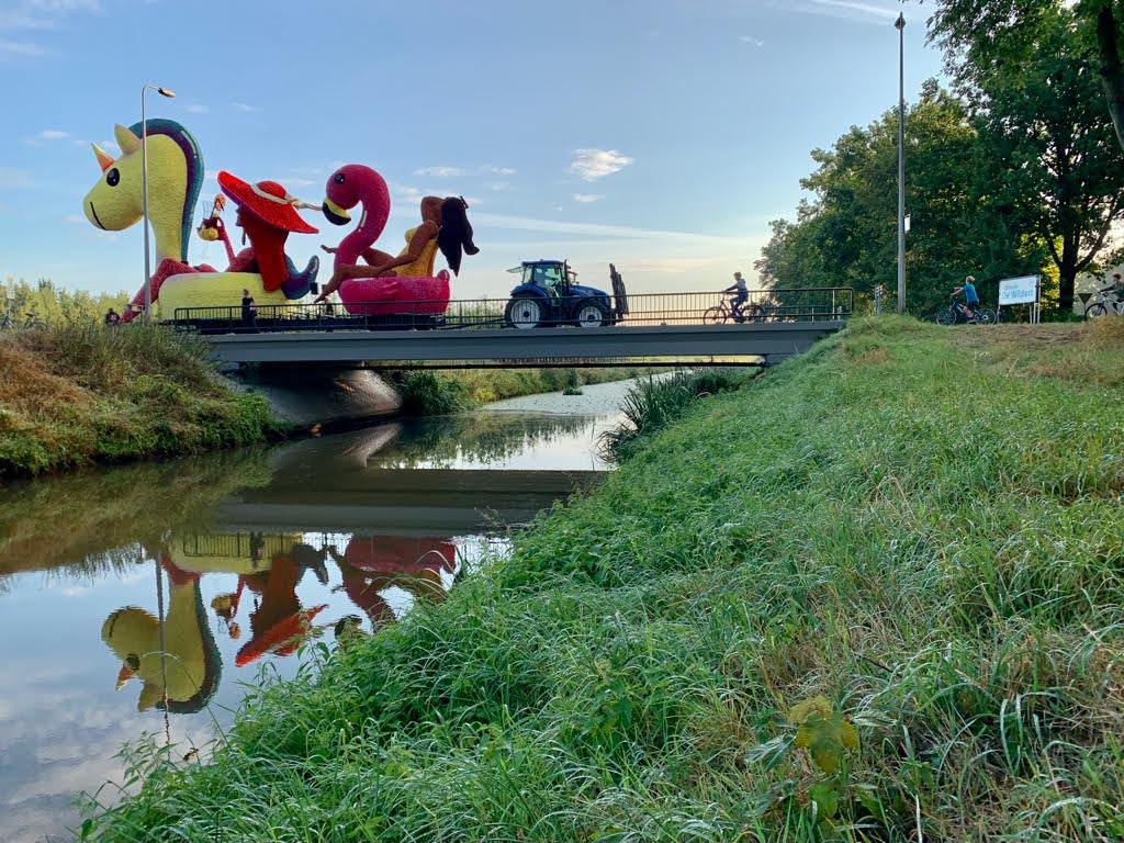 A small farm tractor crossing a small bridge tows a large parade float behind it.