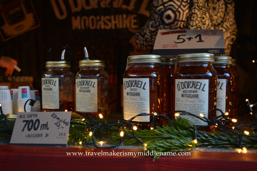 Glass jars of an alcoholic drink called "Moonshine" on a table at a Christmas market stall decorated with lights
