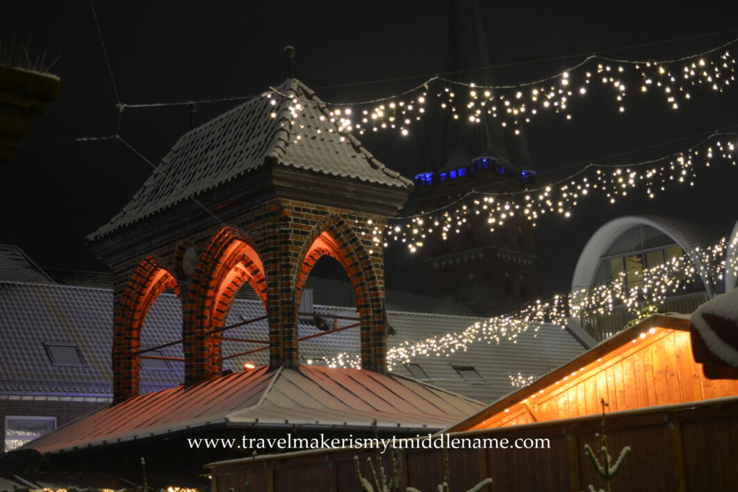 Night time: A cupola on a roof dusted with snow and lit with an orange glow of light, with white strings of light hanging from the roof.