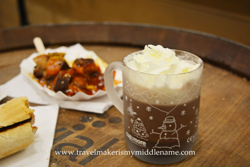 Hot chocolate with whipped cream and sausages in the background on a wooden barrel table