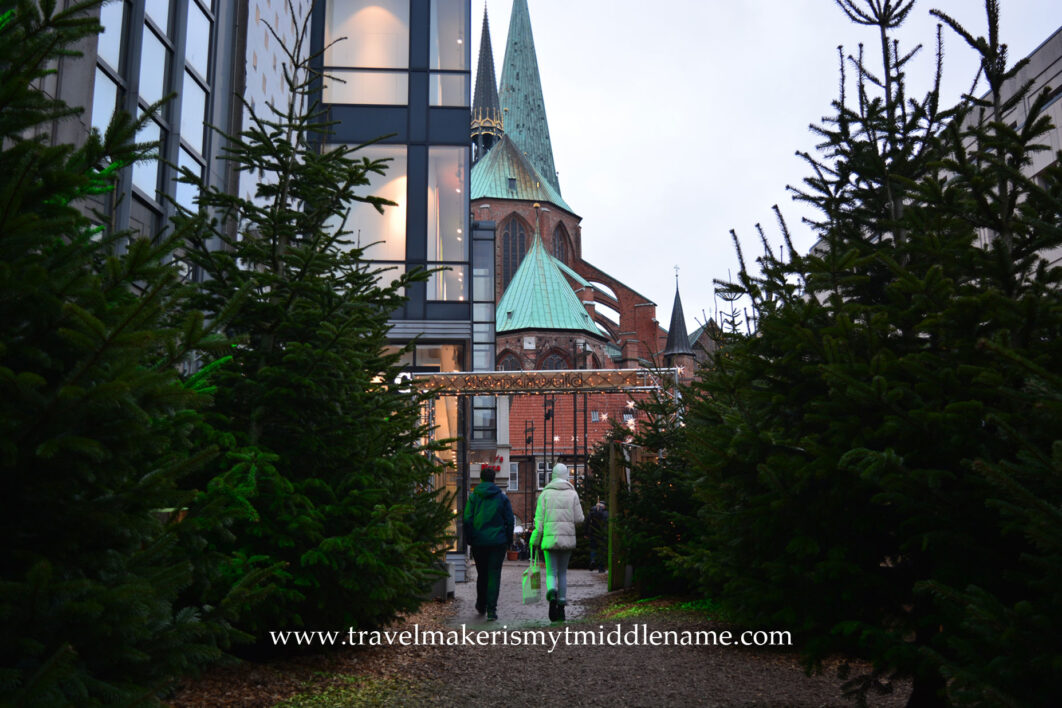 Two people walking in to a Christmas market in Lübeck with a church and buttresses in the background