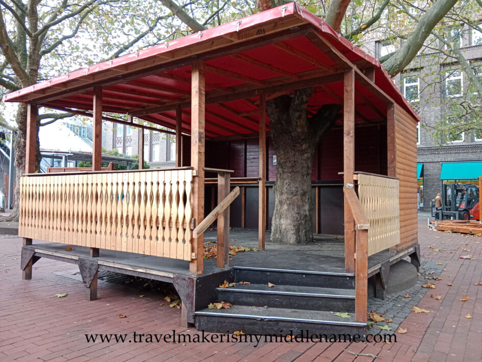 An empty, walk in Christmas market hut with stairs built around a tree trunk in the middle being set up during the day