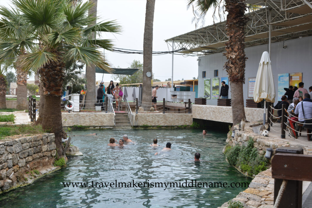 People bathing in the Pamukkale Antique Pool, also called Cleopatra Pool, in Pamukkale, Türkiye. Lockers and change rooms are in the background.