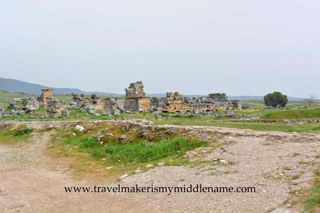 A cloudy day. Stone ruins in the background among the hilly natural landscapes covered in green grass in Pamukkale in Turkiye.