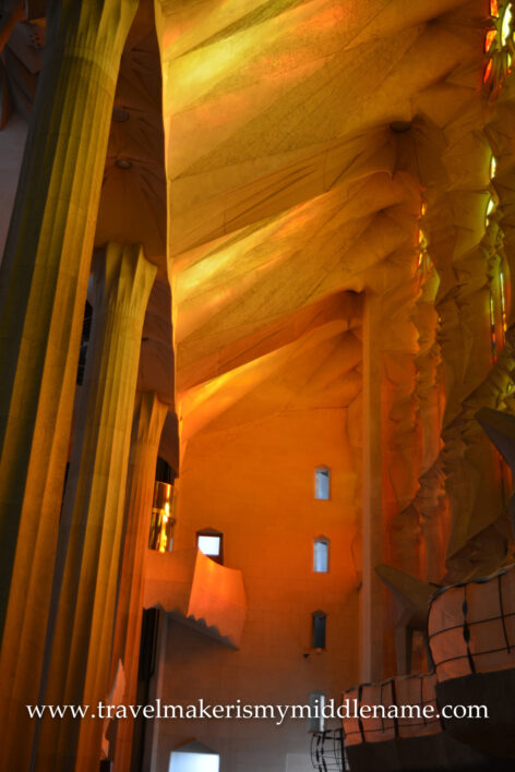 Afternoon sunlight that shines through the red, yellow, and orange stained glass inside La Sagrada Familia church in Barcelona, Spain reflects off the ceiling.