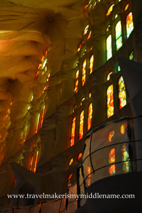 Afternoon sunlight shines through the red, yellow, and orange vertical stained glass windows at ground level inside La Sagrada Familia church in Barcelona, Spain.