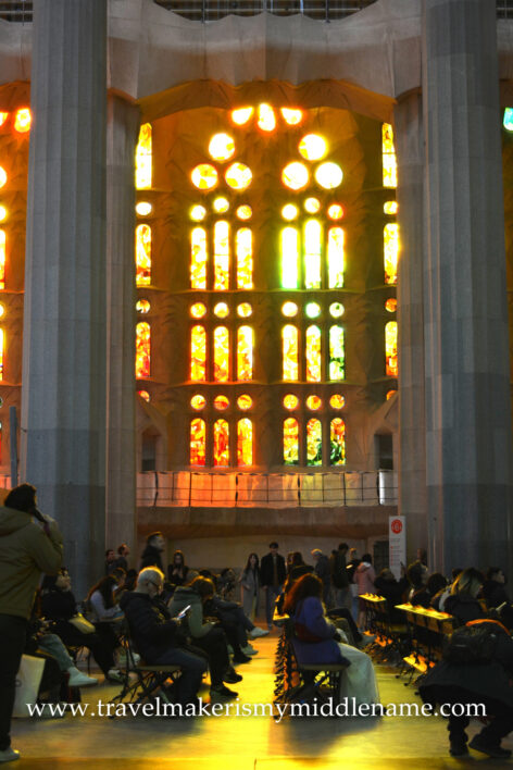 Afternoon sunlight shines through the red, yellow, and orange vertical stained glass windows at ground level inside La Sagrada Familia church in Barcelona, Spain.