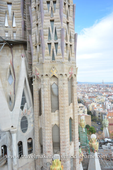 View of the side of a tower and colourful fruit sculptures of La Sagrada Famiila church in Barcelona, Spain, at the tower height. Yellow and green fruit sculptures can be seen in the bottom right corner.