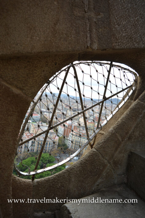 A small liver-shaped cutout from the stone wall at the step level and covered with a metal grate inside the Passion tower of La Sagrada Familia church in Barcelona, Spain, provides some light to where you are stepping and a tiny view to the city outside.