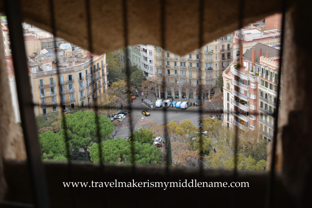 A view of the streets and buildings in Barcelona below from La Sagrada Familia church in Barcelona, Spain, as seen from the top of the Passion tower through window openings cut in the tower wall, covered with a small metal grate.