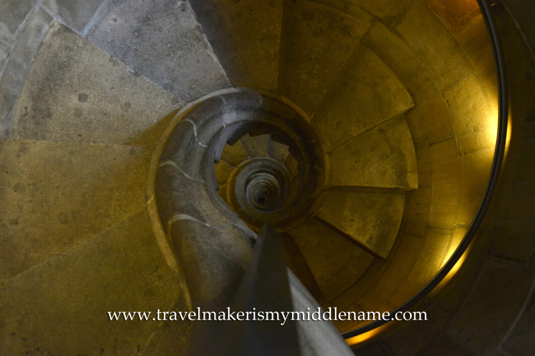 Downwards view of the internal spiral staircase of the Passion tower in La Sagrada Familia church in Barcelona, Spain. It is dimly lit and the stone stairs wind downwards in an anti-clockwise direction.