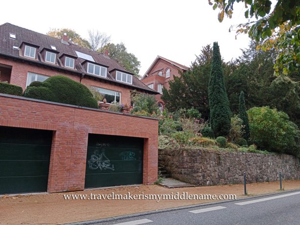 A residential red brick building with a green double garage and a small stone walled garden containing various green plants.