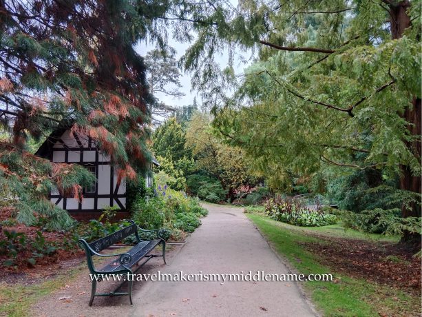 A half timbered house, park bench, and a footpath amongst green tree canopy