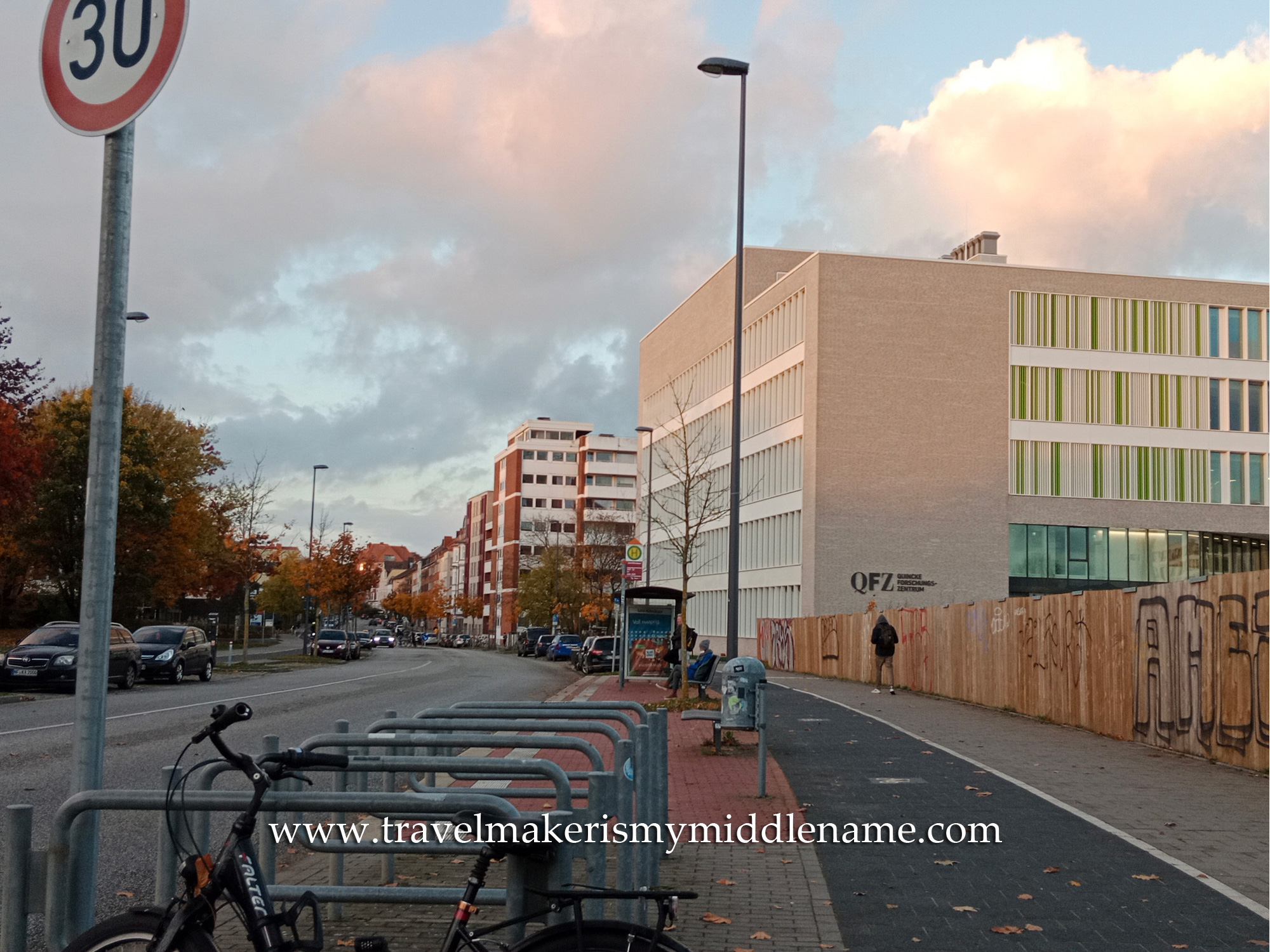 A modern, light brick cube building on the right hand side with a foot and bike path on the outside.