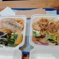 Two packs of grilled fish fillets with salad, lemon, and hot potato chips