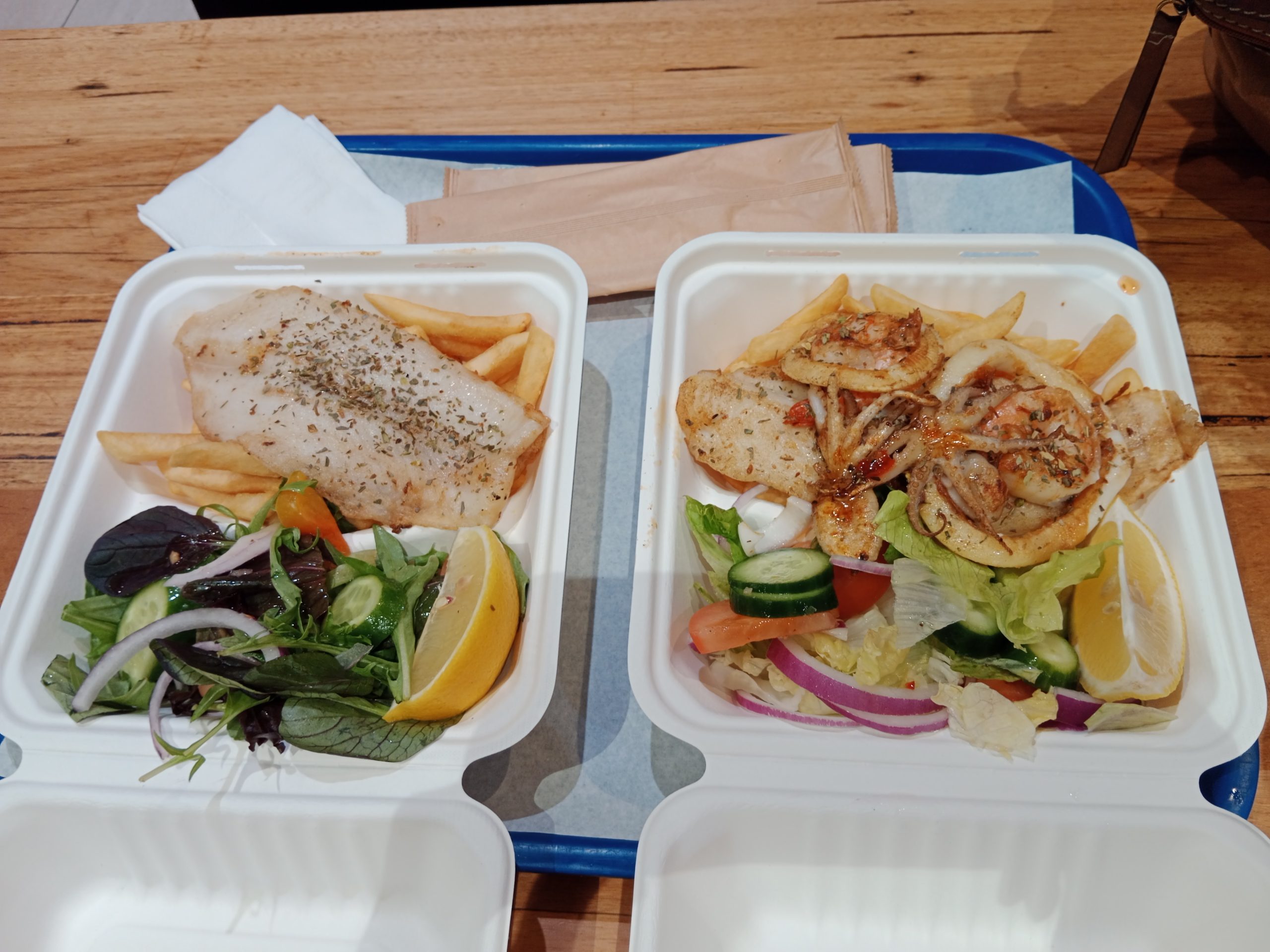 Two packs of grilled fish fillets with salad, lemon, and hot potato chips